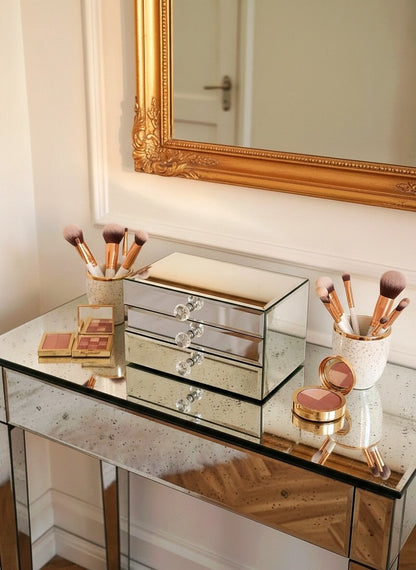 Mirror organizer with 2 drawers by Mirrorina on an antique mirrored table, styled with gold-framed mirror behind, makeup palettes on both sides, and brushes in white cups.