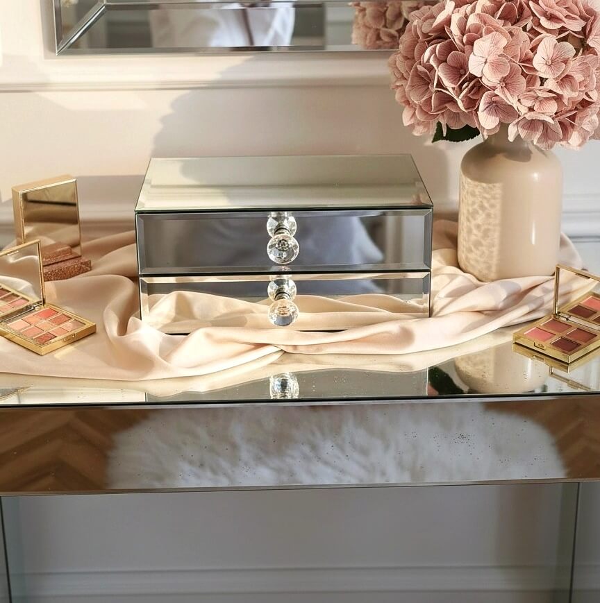 Mirror organizer with 2 drawers by Mirrorina on a mirrored console, styled with a vase of pink hydrangeas on the right and makeup palettes on the left.