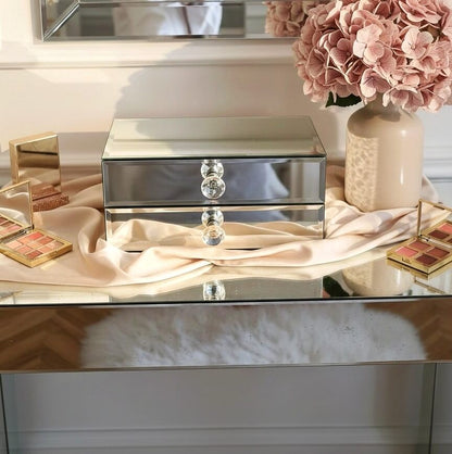 Mirror organizer with 2 drawers by Mirrorina on a mirrored console, styled with a vase of pink hydrangeas on the right and makeup palettes on the left.