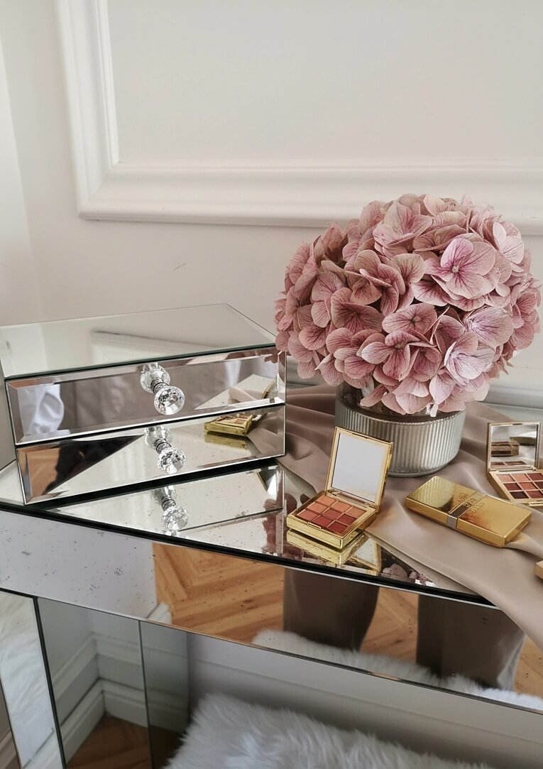 Side view of Mirrorina mirror organizer with 2 drawers on a mirrored console, styled with a vase of pink hydrangeas and makeup palettes on the right.